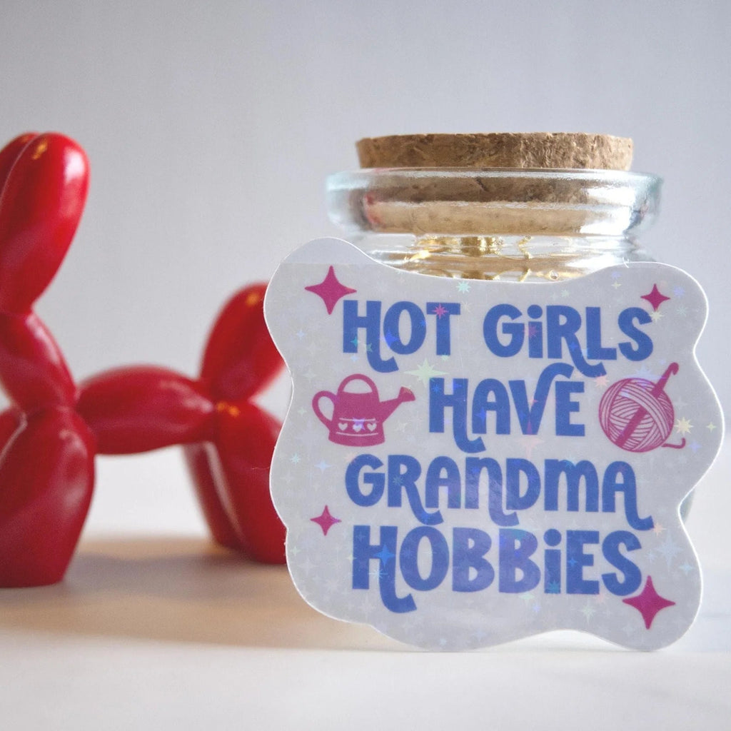 Glass jar with cork lid and 'Hot girls have grandma hobbies' sticker, red balloon dog toy in the background.