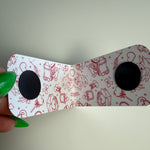 White magnetic bookmark with red illustrations held by a hand against a plain background