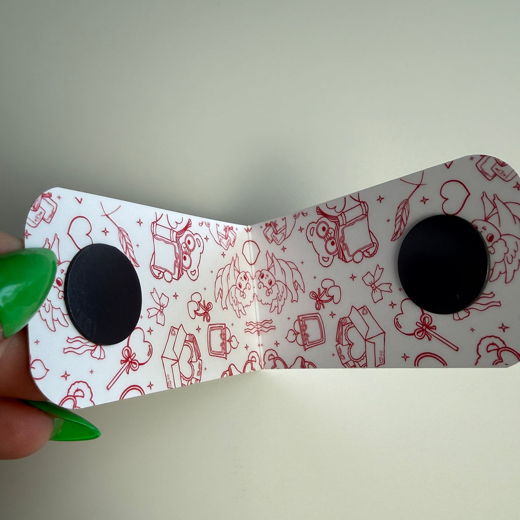 White magnetic bookmark with red illustrations held by a hand against a plain background