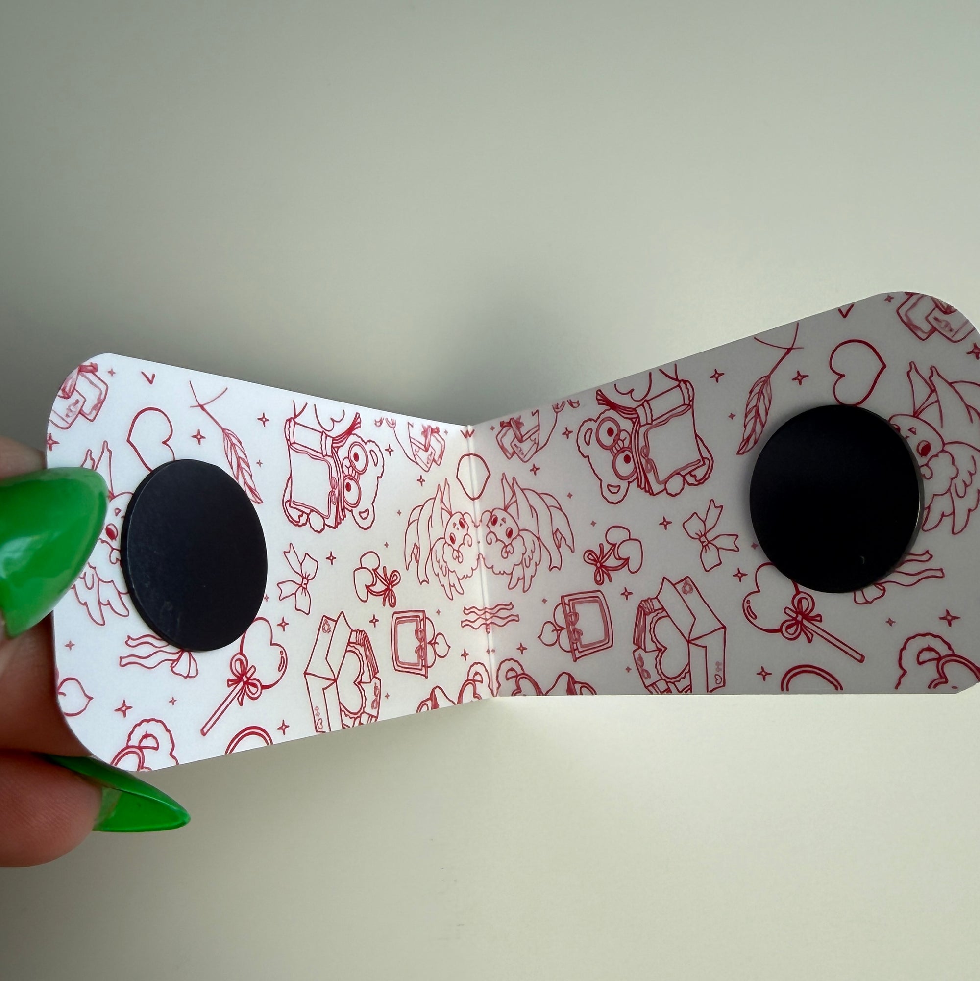 White magnetic bookmark with red illustrations held by a hand against a plain background