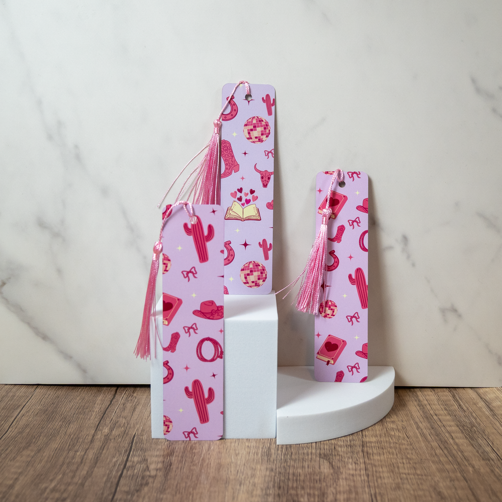 3 bookmarks with pink tassel on a white pedestal against a marble background