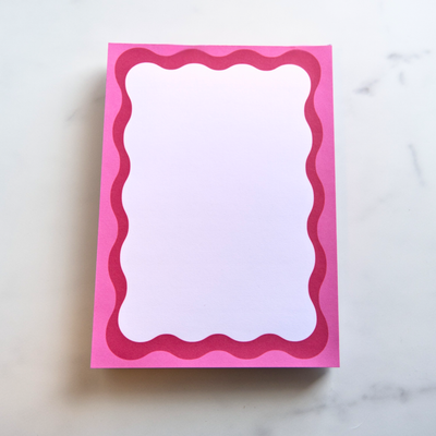 Pink notepad with wavy border on a white marble surface