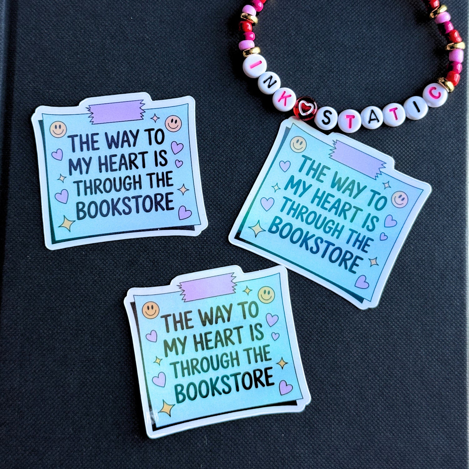 Three blue stickers with text on a black background, featuring a colorful beaded necklace.