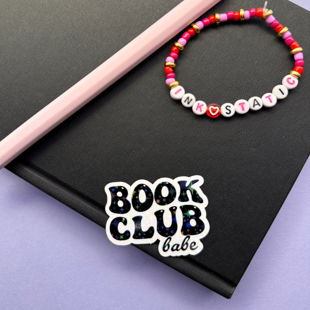 Colorful beaded bracelet with letter beads on a black notebook with 'Book Club Babe' sticker.