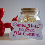 Glass jar with gold paper clips and a sign reading 'Curbs Hate to See Me Coming' next to a red balloon dog.