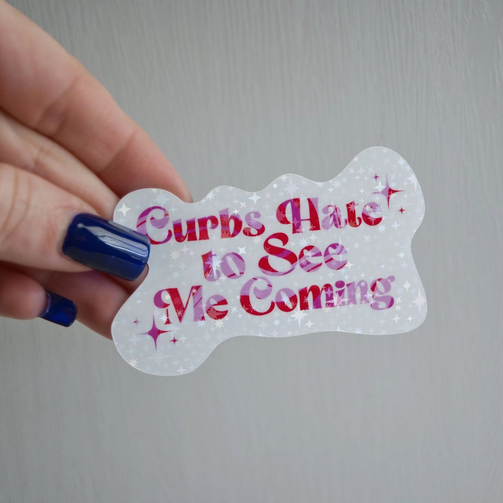Hand holding a transparent sticker with red text on a gray background
