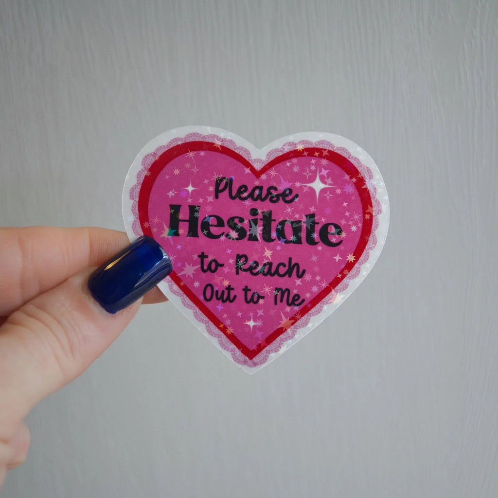 Heart-shaped sticker with text held by a hand against a plain background