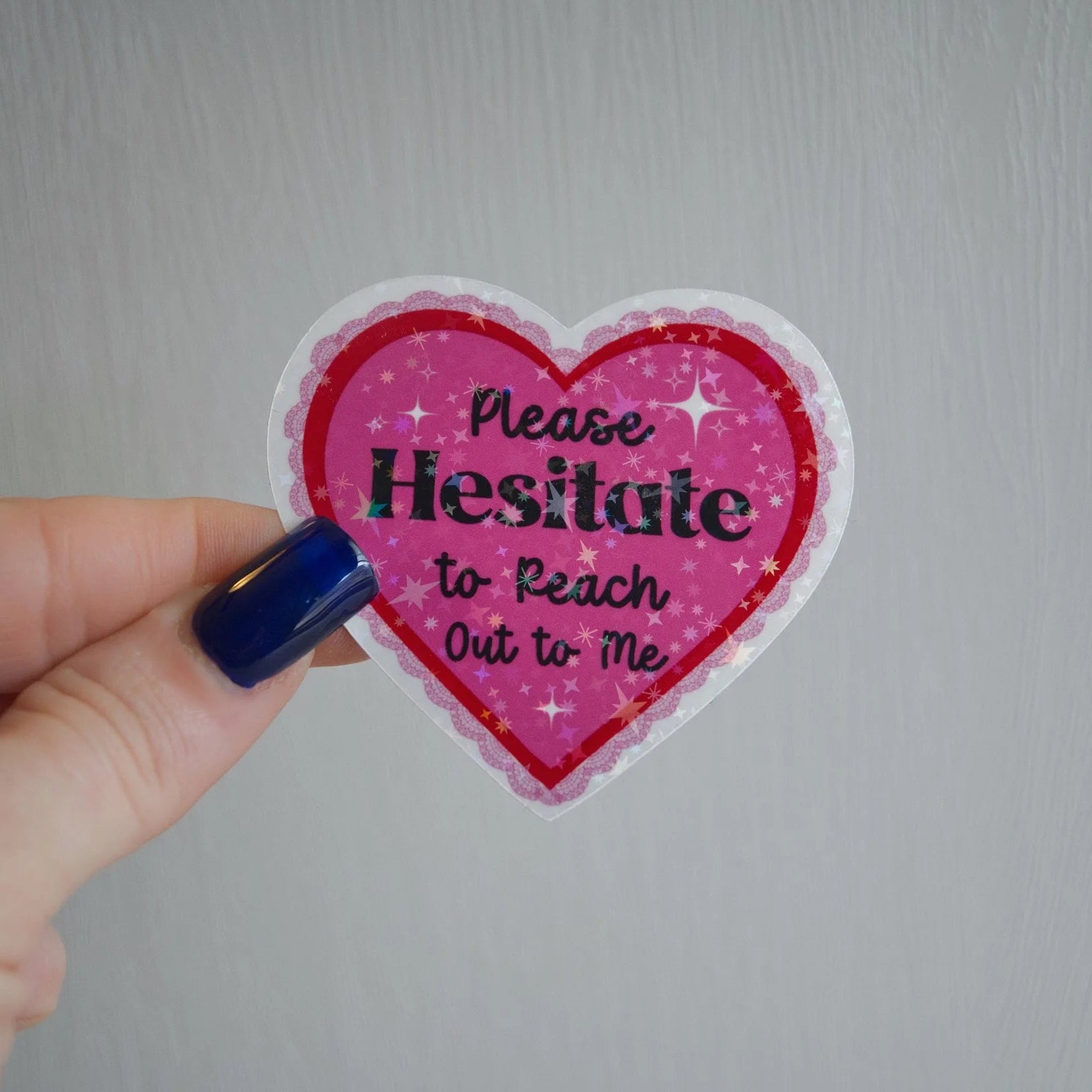 Heart-shaped sticker with text held by a hand against a plain background