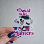 Sticker with cartoon coffee cup character and text 'Decaf is for Quitters' held by a hand.