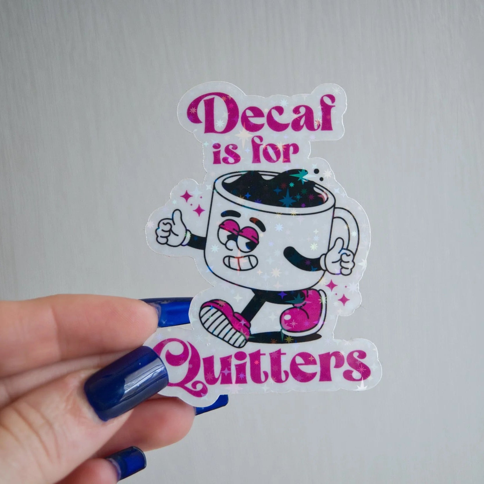 Sticker with cartoon coffee cup character and text 'Decaf is for Quitters' held by a hand.