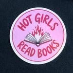Pink round sticker with text 'Hot girls read books' on a dark background