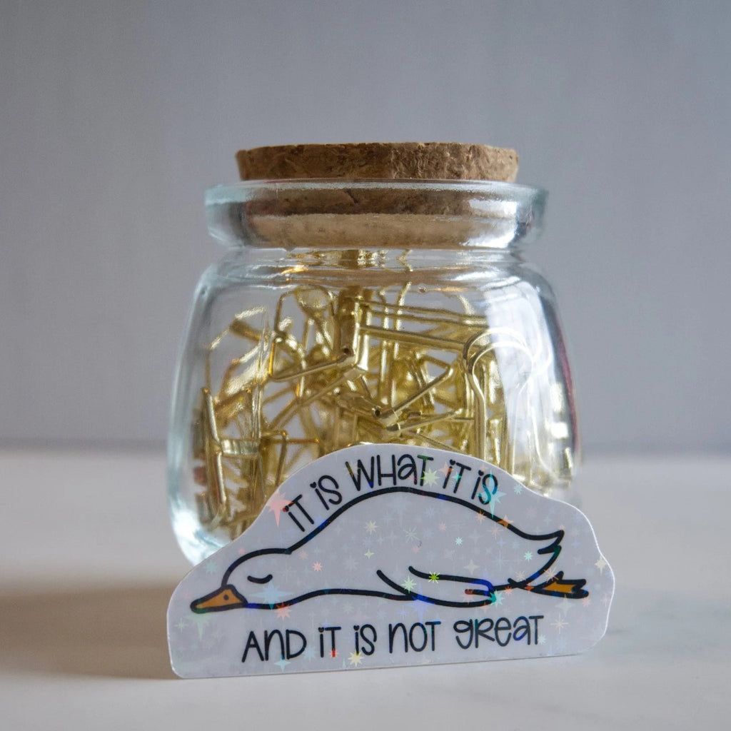 Jar of gold paper clips with a sticker on a white surface