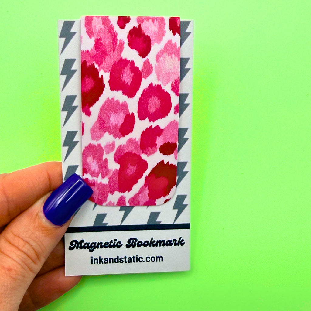 Magnetic bookmark with pink leopard print design held by a hand against a green background