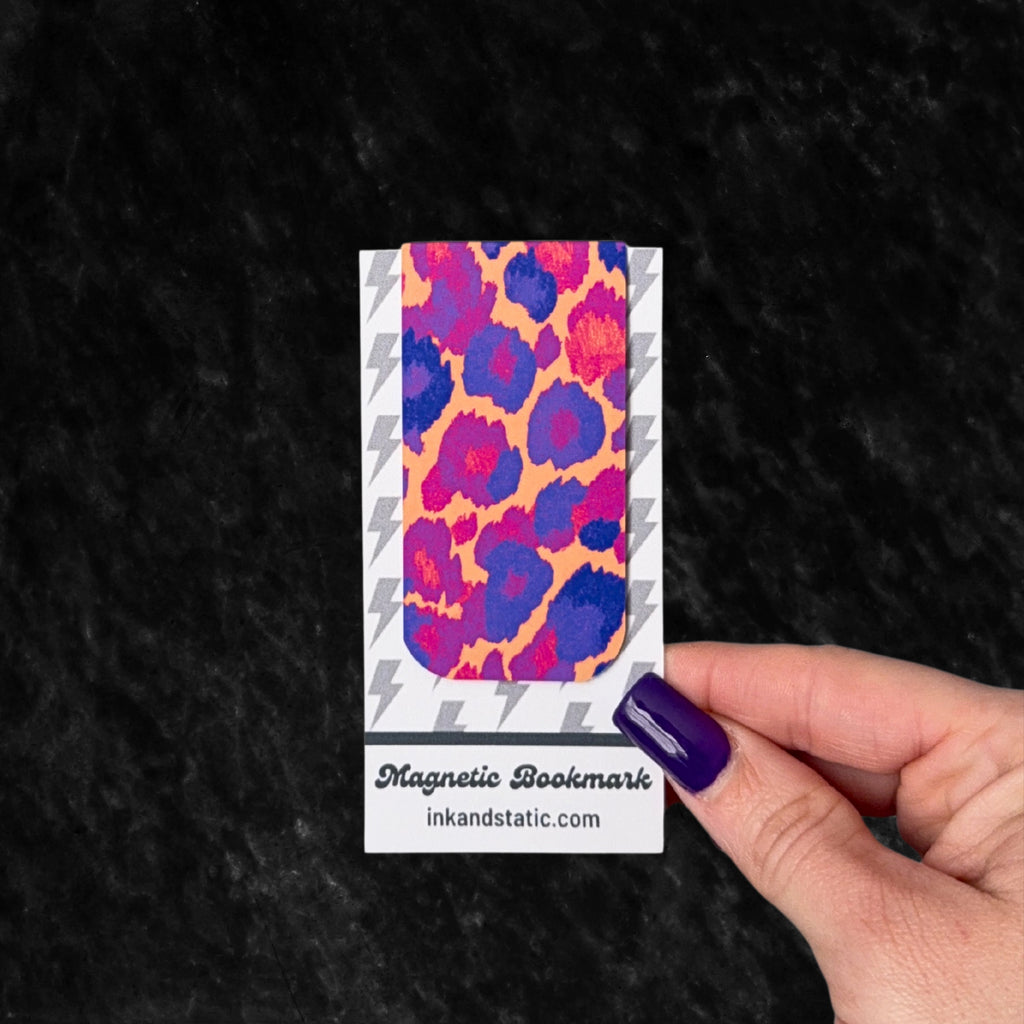 Magnetic bookmark with colorful leopard print design held by a hand against a black background
