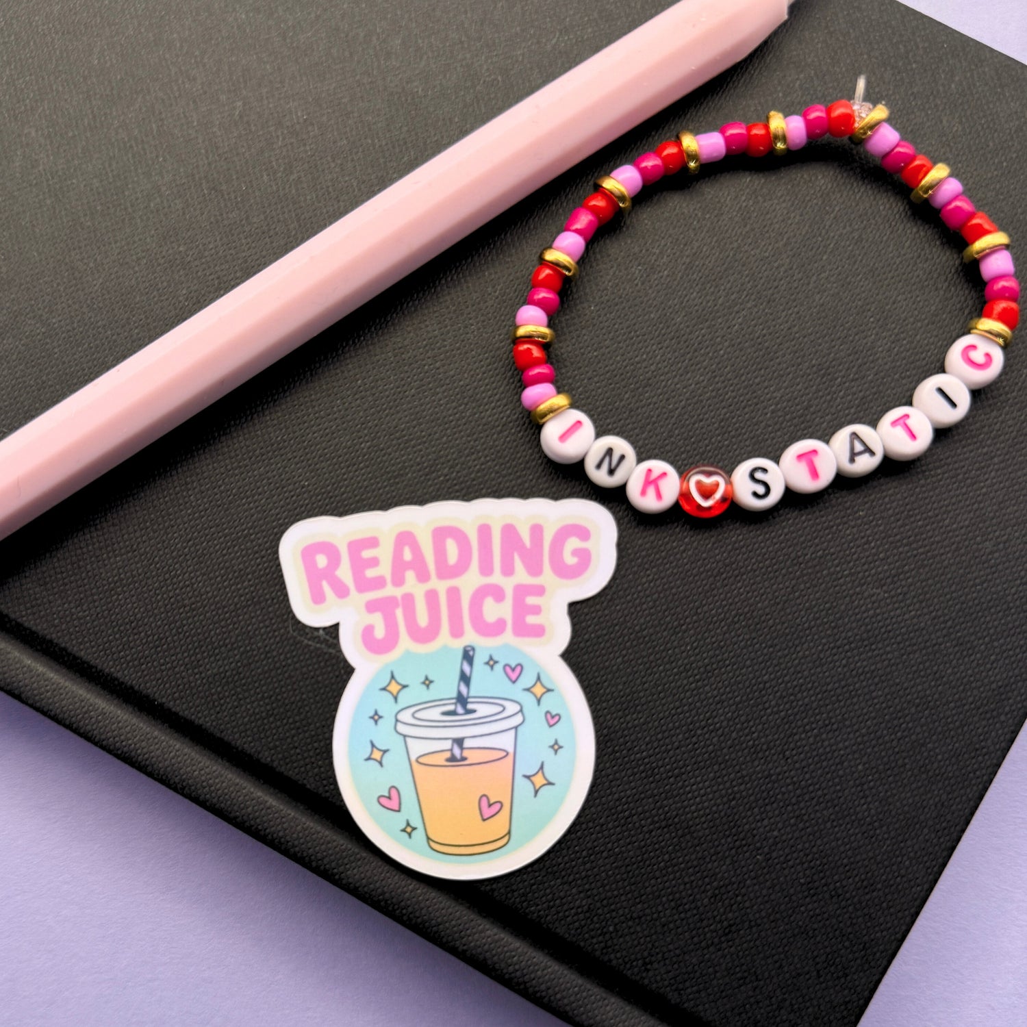 Colorful beaded bracelet and 'Reading Juice' sticker on a black surface with a pink pen.