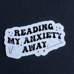 Sticker with 'Reading my anxiety away' text on a dark background
