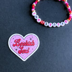 Heart-shaped 'Bookish Soul' sticker with a beaded bracelet on a dark background