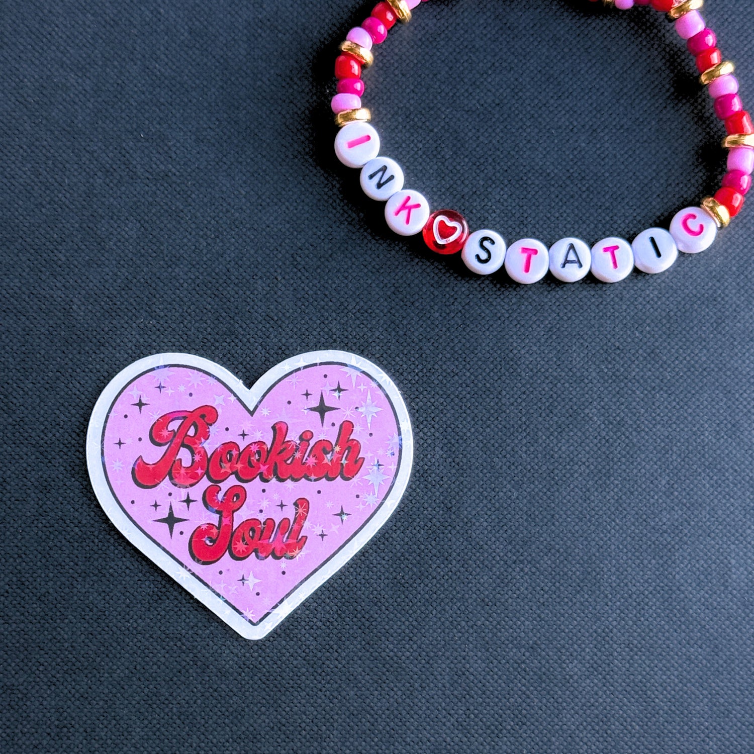Heart-shaped 'Bookish Soul' sticker with a beaded bracelet on a dark background
