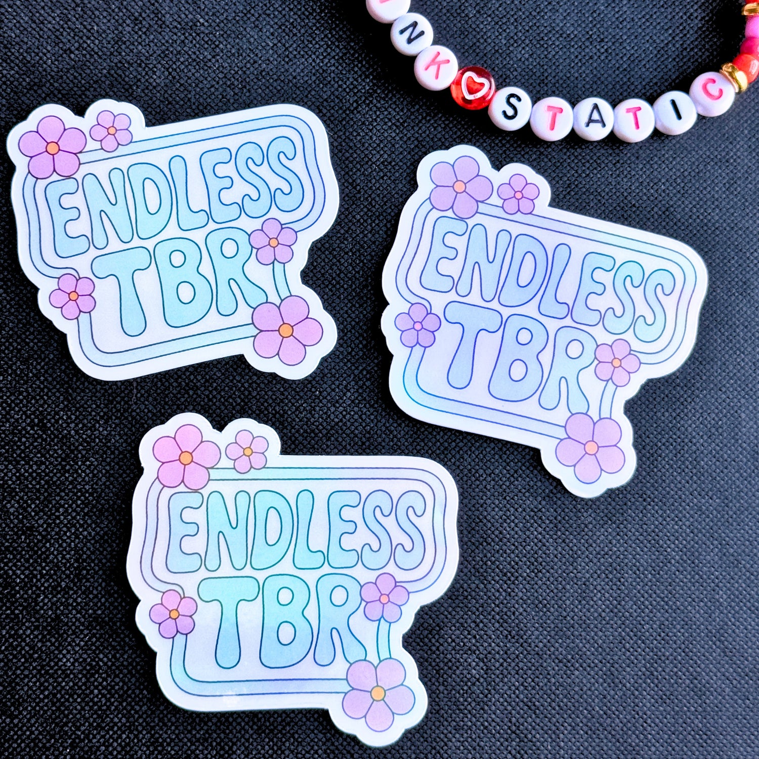 Three 'Endless TBR' stickers with floral designs on a dark fabric background.