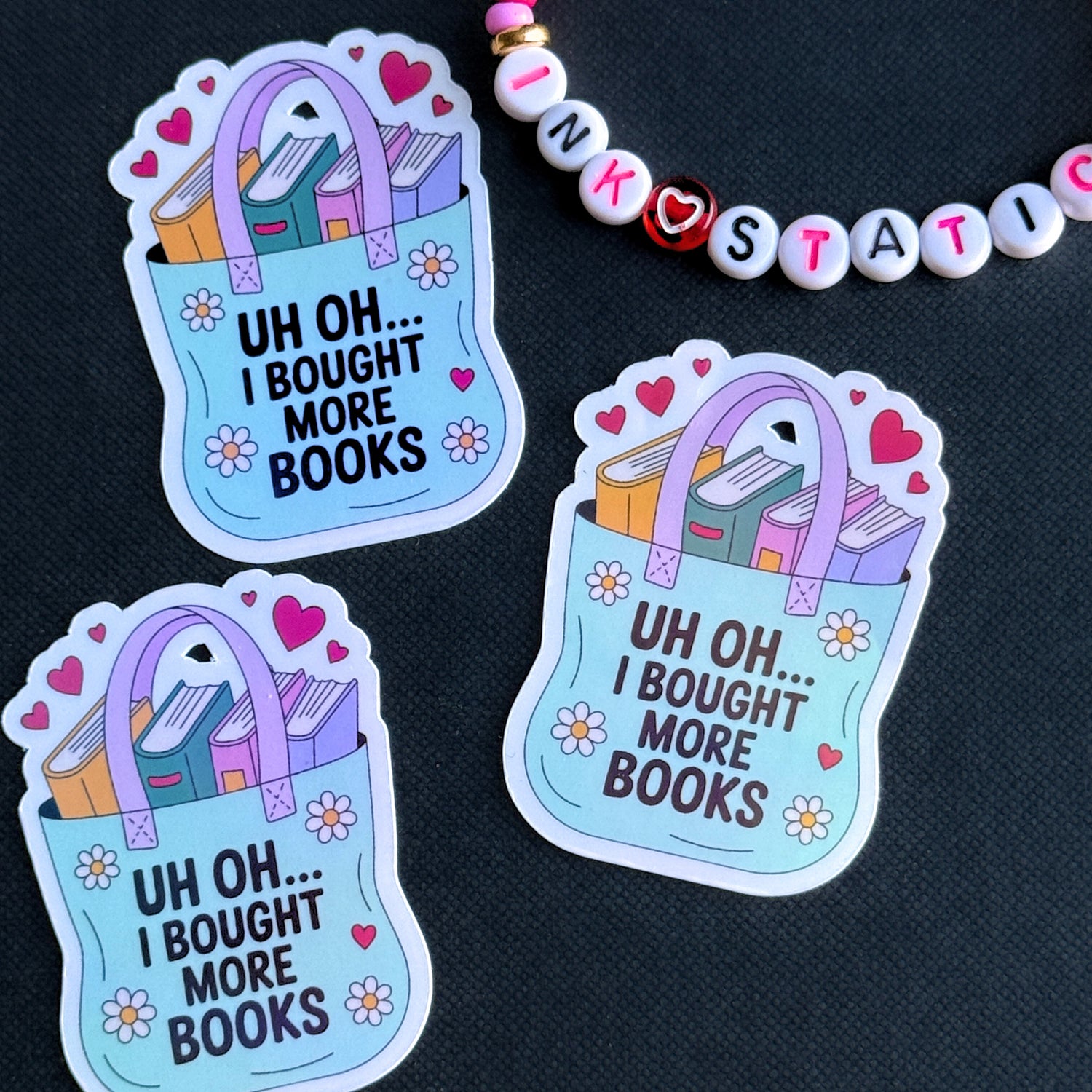 Three stickers with a book bag design and text 'Uh oh... I bought more books' on a dark background.